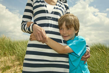 Son embracing mother standing at beach - AJOF01590