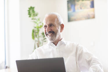 Happy businessman with laptop looking away in office - SGF02868