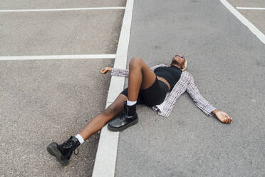 Carefree woman with arms outstretched lying on road in city - MEUF03947