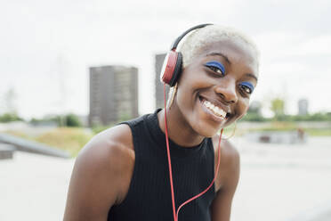 Happy woman listening music through headphones at park - MEUF03963