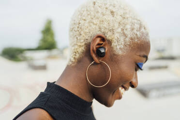 Lächelnde junge Frau mit drahtlosen In-Ear-Kopfhörern im Park - MEUF03964