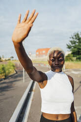 Frau winkt mit der Hand, während sie an einem sonnigen Tag auf der Straße steht - MEUF03974