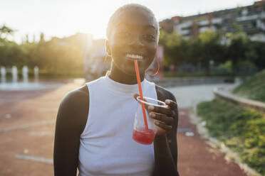 Lächelnde Frau mit Smoothie in der Hand im Park stehend - MEUF03999