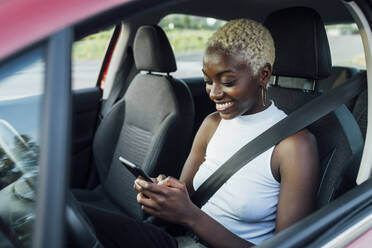 Lächelnde Frau, die ein Mobiltelefon benutzt, während sie im Auto sitzt - MEUF04004