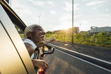 Cheerful young woman leaning on window of car - MEUF04007