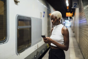 Junge Frau benutzt ein Mobiltelefon, während sie in einer U-Bahn-Station steht - MEUF04014