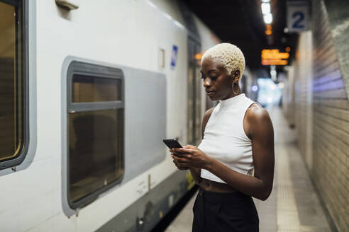 Junge Frau benutzt ein Mobiltelefon, während sie in einer U-Bahn-Station steht - MEUF04014