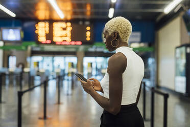 Junge Frau benutzt ihr Smartphone, während sie in der U-Bahn-Station steht - MEUF04020