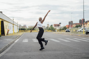 Lächelnde Frau mit erhobener Hand tanzt auf der Straße in der Stadt - MEUF04021