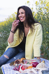 Lächelnde Frau, die auf einem Feld sitzend Früchte isst - PNAF02110