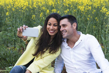 Happy couple taking selfie through smart phone in field - PNAF02113