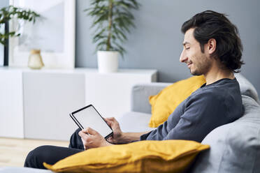 Man using digital tablet while sitting on sofa - BSZF01810