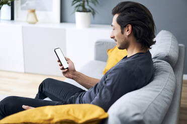 Man using mobile phone while sitting on sofa at home - BSZF01813