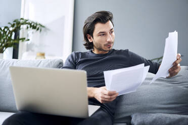 Male professional looking at documents while sitting at home - BSZF01824