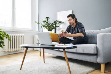 Male professional during video call on laptop while sitting on sofa at home - BSZF01834