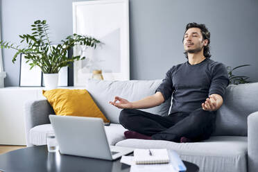 Male professional meditating while sitting on sofa at home - BSZF01838