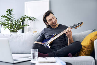 Mann spielt E-Gitarre, während er zu Hause auf dem Sofa sitzt - BSZF01840