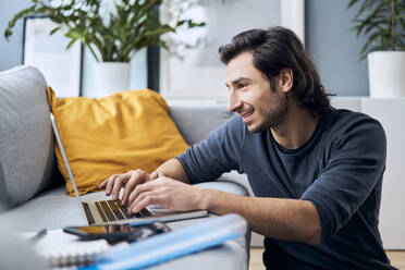 Männlicher Freiberufler mit Laptop auf dem Sofa bei der Arbeit zu Hause - BSZF01853