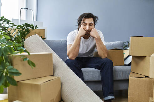 Aufgeregter Mann sitzt auf dem Sofa inmitten von Kartons zu Hause - BSZF01867