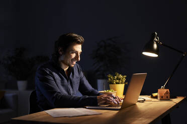 Männlicher Berufstätiger mit Laptop am Schreibtisch bei der Arbeit zu Hause - BSZF01876