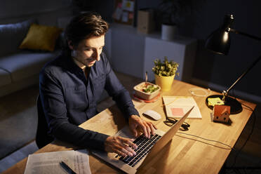 Männlicher Freiberufler, der bis spät in die Nacht im Home Office arbeitet - BSZF01877