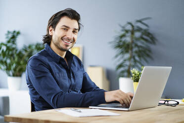 Male freelance worker with laptop on desk at home office - BSZF01883