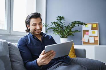 Lächelnder Geschäftsmann mit digitalem Tablet auf dem Sofa im Büro - BSZF01890