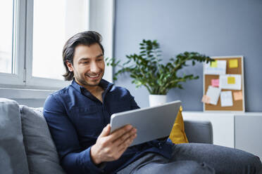 Smiling businessman using digital tablet on sofa at office - BSZF01890