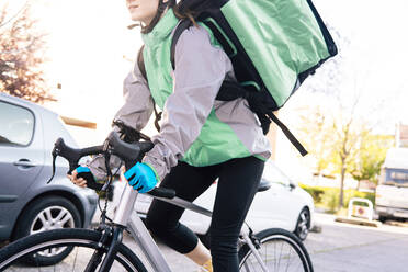 Niedrige Winkel Ernte der weiblichen Kurier mit thermischen Tasche Radfahren auf der Straße während der Lieferung auf sonnigen Tag in der Stadt - ADSF28451