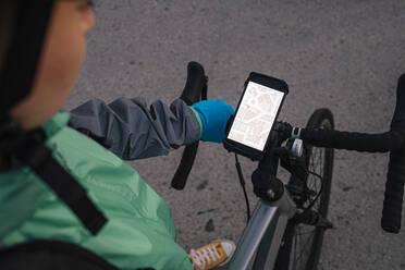 Von oben: anonymer Kurier, der seine Route auf einer GPS-Karte prüft, bevor er mit dem Fahrrad auf der Straße fährt - ADSF28457