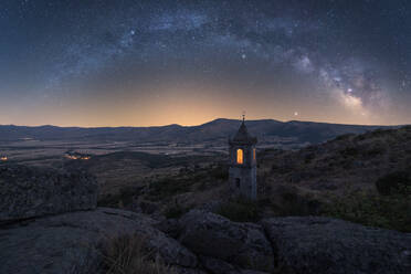 Amazing scenery with aged stone chapel in mountainous valley under evening sky with Milky Way and sunset light - ADSF28466