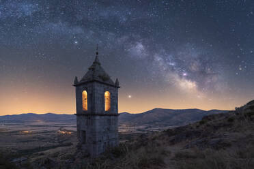 Amazing scenery with aged stone chapel in mountainous valley under evening sky with Milky Way and sunset light - ADSF28471