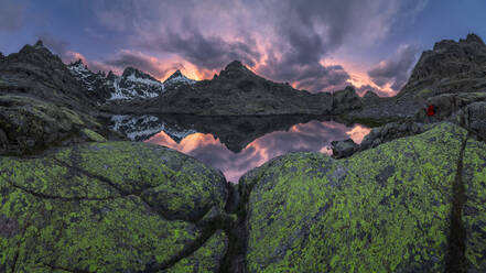 Der See Laguna Grange mit ruhigem Wasser im Circo de Gredos-Karst, umgeben von schneebedeckten Bergkämmen und einem wolkenverhangenen Himmel in Avila, Spanien - ADSF28490