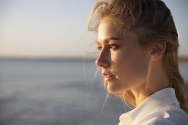 Langhaarige blonde Frau steht am Strand und schaut in die Ferne - ADSF28510