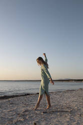 Blonde woman with long hair standing on the beach looking away - ADSF28513