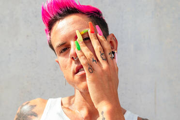 Confident gay male with long colorful nails looking at camera in street on sunny day - ADSF28529