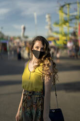 Delighted female in protective mask during coronavirus looking at camera while spending weekend at fairground - ADSF28558