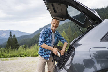 Smiling man packing bag while standing by car - DIGF16305