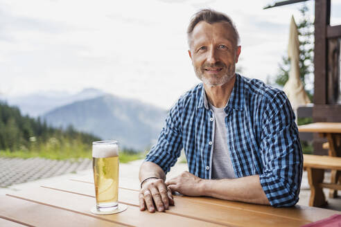 Smiling man sitting with beer glass at bar table - DIGF16312