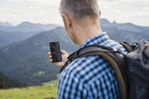 Männlicher Rucksacktourist, der beim Wandern mit seinem Mobiltelefon die Richtung mit Hilfe eines Navigationskompasses sucht - DIGF16317