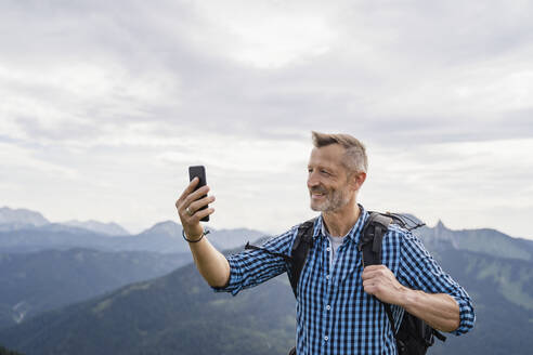 Lächelnder männlicher Rucksacktourist, der ein Selfie mit seinem Mobiltelefon macht - DIGF16318