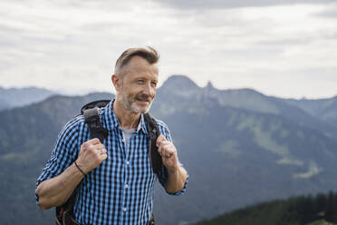 Lächelnder männlicher Rucksacktourist beim Wandern auf einem Berg - DIGF16320