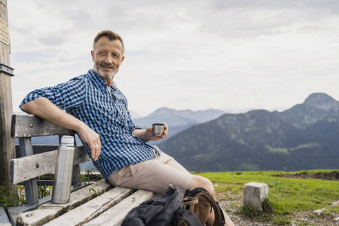 Mann hält Kaffee und sitzt auf einer Bank - DIGF16321