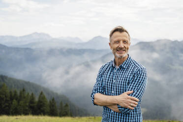 Smiling man with arms crossed standing on mountain - DIGF16331