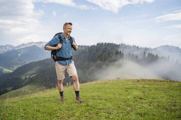 Lächelnder Mann mit Rucksack beim Wandern auf einer Wiese bei nebligem Wetter - DIGF16335