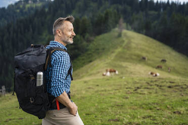 Lächelnder männlicher Wanderer mit der Hand in der Tasche beim Wandern auf einem Berg - DIGF16337