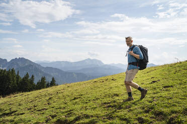 Male hiker with backpack walking down on meadow - DIGF16339