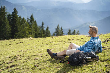 Male hiker resting by backpack on meadow - DIGF16342