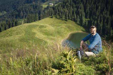 Lächelnder männlicher Wanderer, der sich auf einem Berg sitzend ausruht - DIGF16349