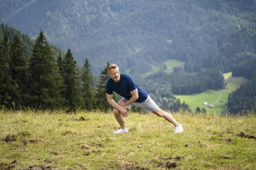Mann streckt die Beine beim Sport auf einem Berg - DIGF16355